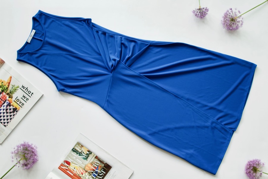 Flatlay of a sleeveless blue dress with gatehring at the waist.