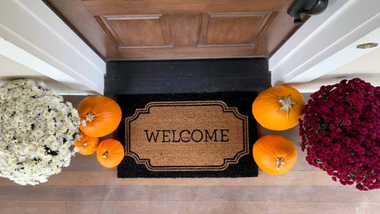 Welcome mat and pumpkins at a brown front door