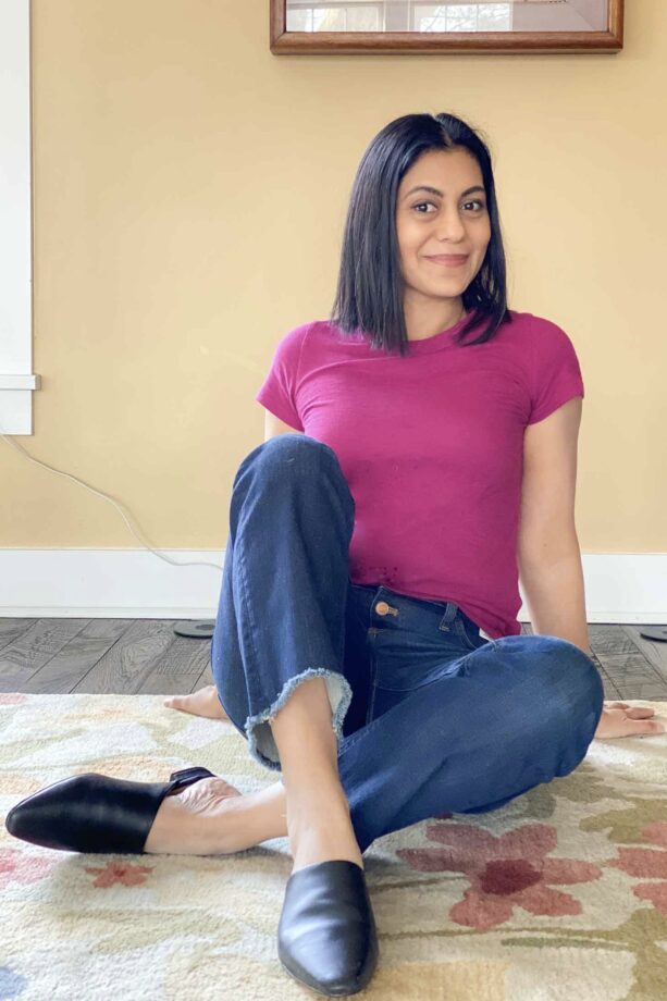Fashionipa sitting down wearing a pink t-shirt, blue jeans and balck mules.