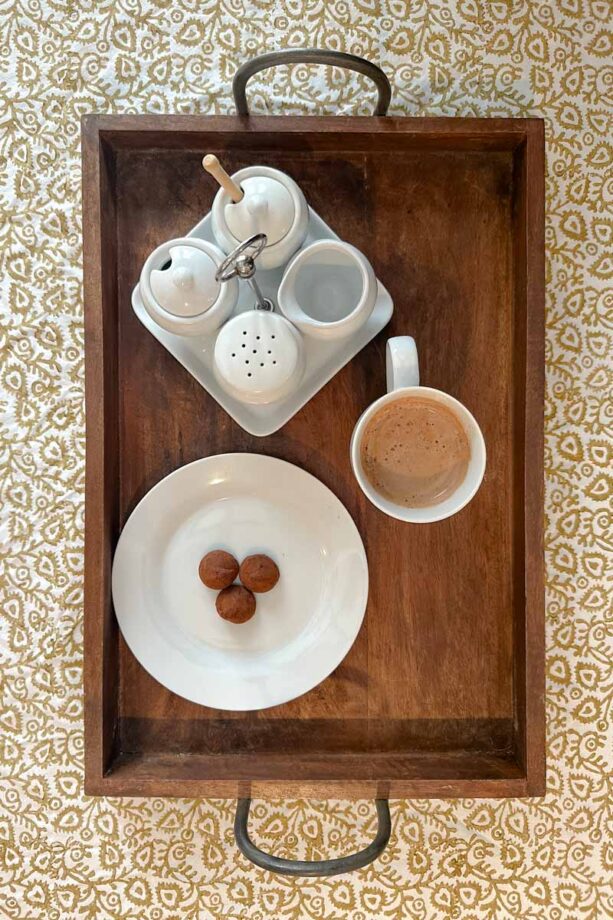 Birdseye view of wooden tray with coffee, a plate of chocolate, and a sugar/creamer set on a square platter.