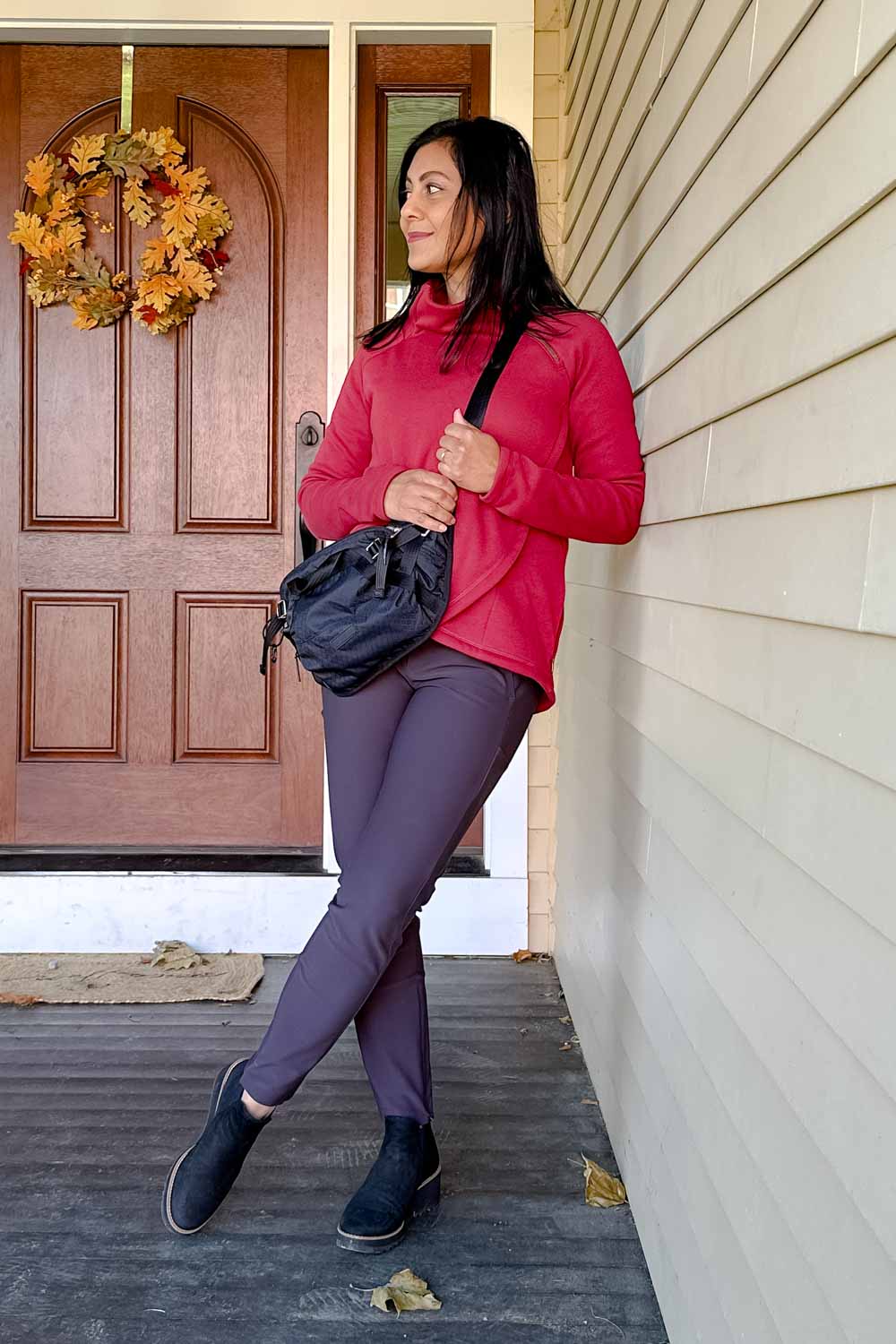Fashionipa (Nipa) standing on a porch wearing a cozy sherpa-lined sweatshirt with gray pants, black boots and a crossbody bag.   