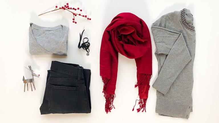 Flatlay of black jeans, gray t-shirt, gray cardigan, red scarf, necklace and holiday decor.