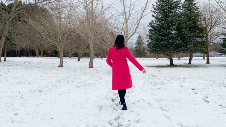 Fashionipa walking away wearing a hot pink coat, black pants and boots.