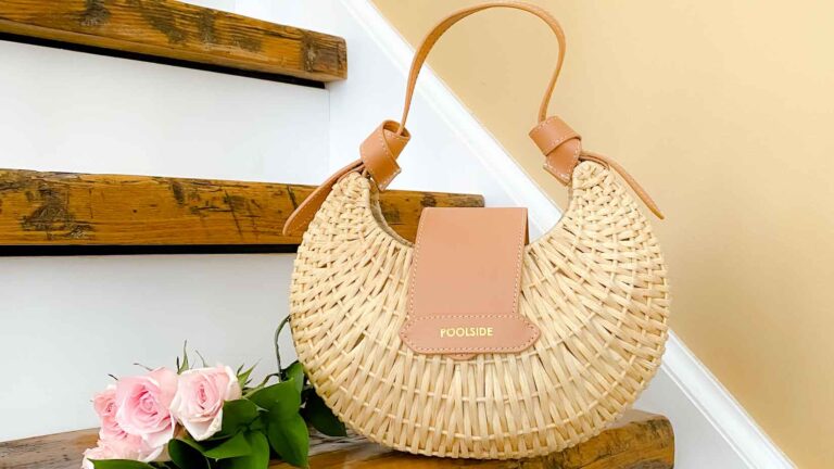 Round wicker handbag on wooden steps next to pink roses
