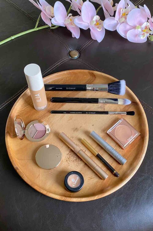 Foundation, brushes, eyeshadow, concealer, mascara, eyeliner and highlighter on a round wooden tray