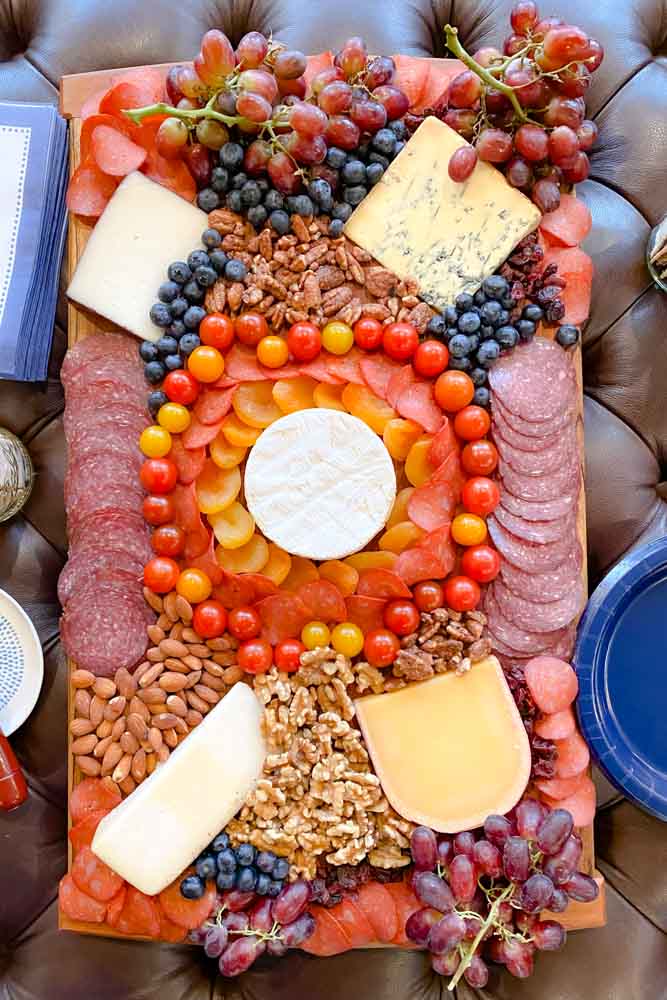 Large charcuterie board with meat, cheese, tomatoes, grapes and nuts.