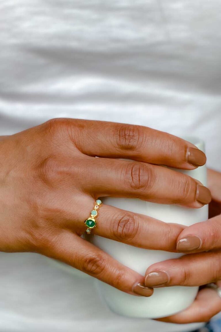 Woman's hand wearing a gold vermeil ring with green stones.
