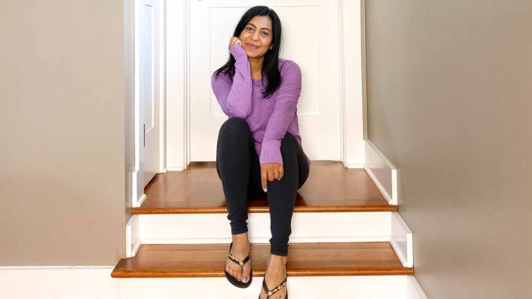 Fashionipa sitting on steps wearing a lilac long-sleeved t-shirt, black leggings and flip-flops