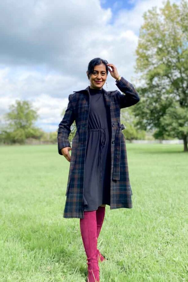 Fashionipa (Nipa) wearing a brown and black plaid coat, black dress and burgundy knee-high boots outside in a an open field.