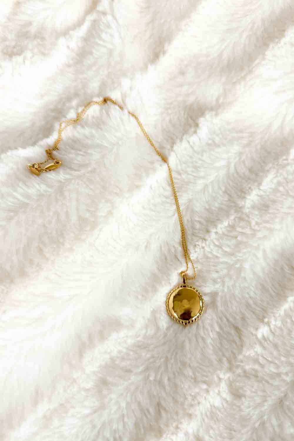 Image of a gold locket and chain on a white blanket.