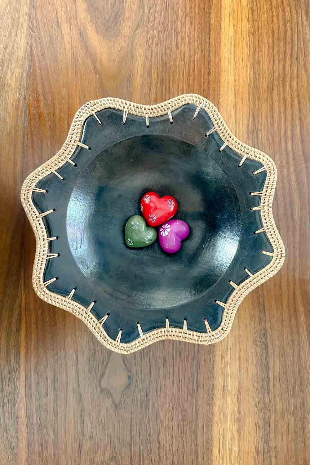 Red, green and purple engraved soapstone hearts in a bowl with woven thread edges.