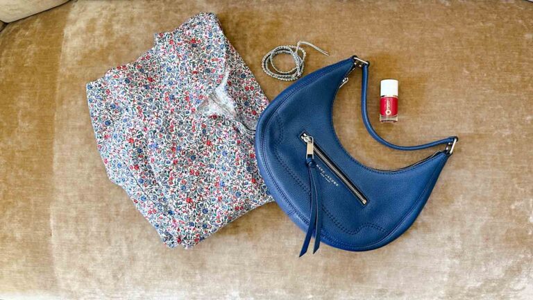 Image of a red, white and blue floral print dress, a blue handbag, red nail polish and a blue and gray wrap bracelet.