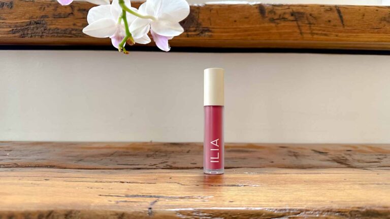 Ilia Balmy Gloss tinted Lip Oil in a dark pink on a distressed wooden staircase.