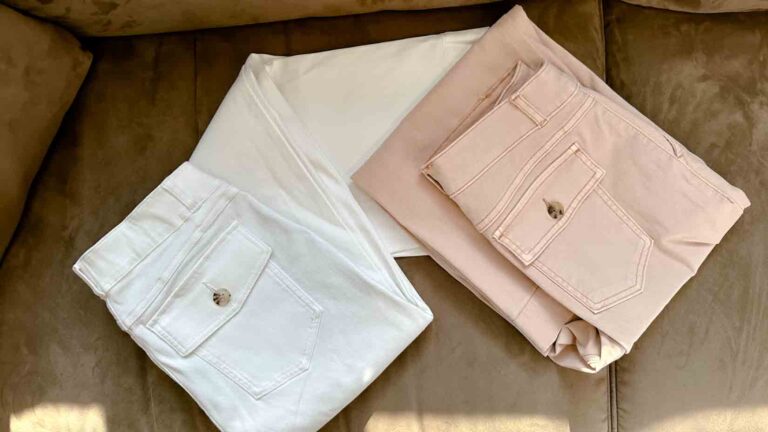 Two pairs of Spanx® wide-leg cropped pants on a tan couch. One pant is white, the other pale pink.