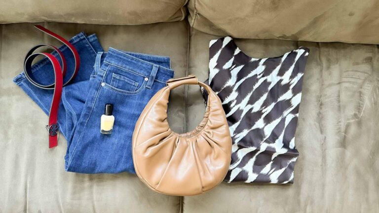Image of a red belt, blue jeans, yellow nail polish, a tan handbag and a brown and white print top ona. tan couch.