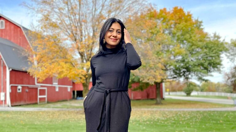 Fashionipa (Nipa) wearing a black dress standing in front of a red barn and fall trees.