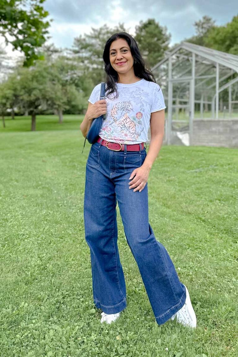 Fashionipa (Nipa) wearing wide leg jeans with patch pockets, white sneakers, a graphic t-shirt, a magenta belt, carrying. blue crescent handbag.