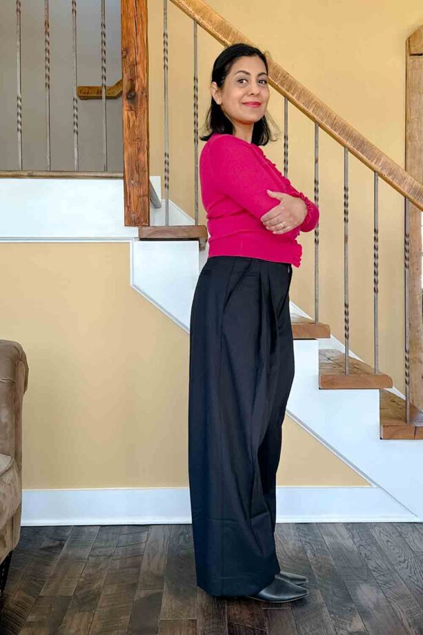 Fashionipa (Nipa) standing in front of a staircase wearing a pink sweater and voluminous black pants.