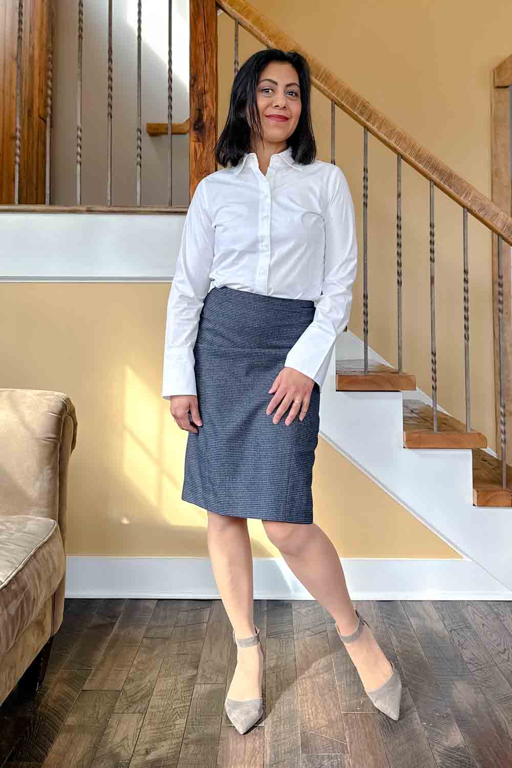 Fashionipa (Nipa) standing in front of a staircase wearing a white blouse and dark blue pencil skirt.