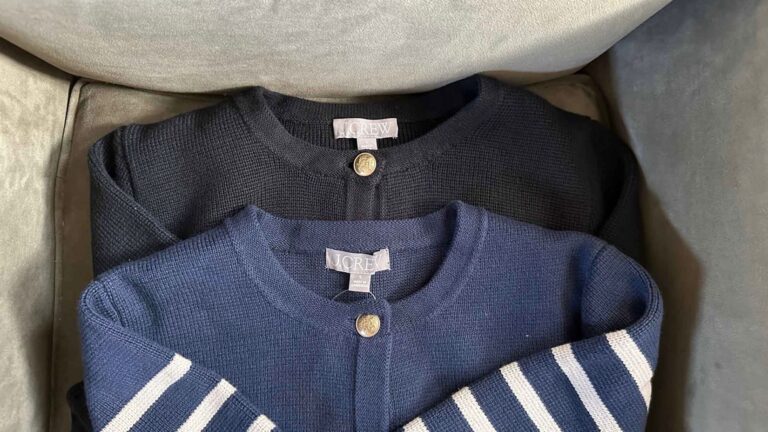 Image of two J.Crew sweater jackets on a plush chair, one black, the other navy striped.