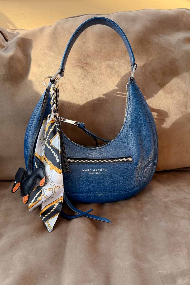 Blue crescent shaped handbag with a dog and scarf bag charm.