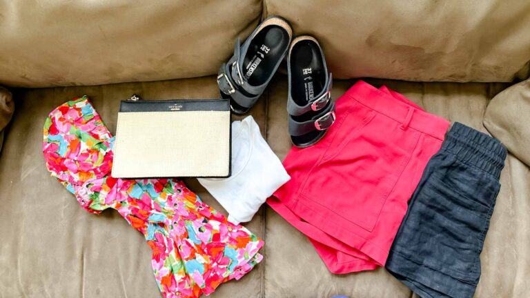 Shorts, printed tops, clutch, sandals and a tank top folded on a tan couch.