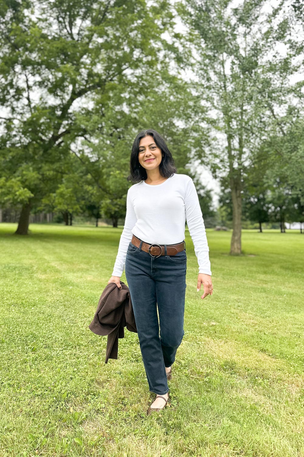 Fashionipa (Nipa) wearing a white long sleeved t-shirt, blue jeans, a brown belt and brown shoes. She is carrying a brown jacket.