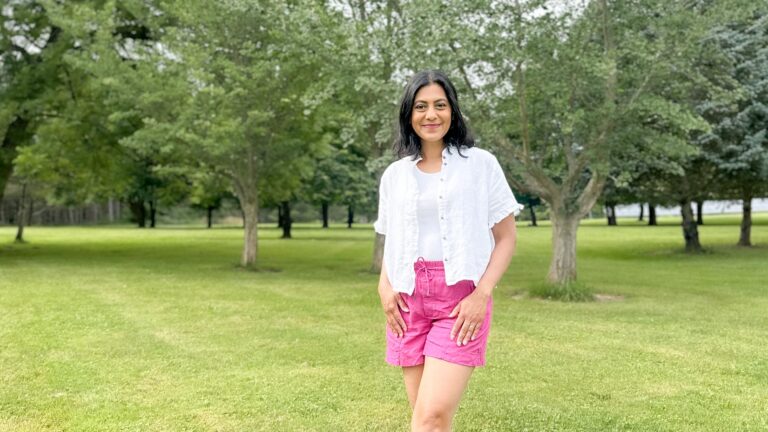Fashionipa (Nipa) standing in a park wearing pink linen shorts, a white tank top and a short sleevd linen shirt with ruffles at the enck and sleeves.
