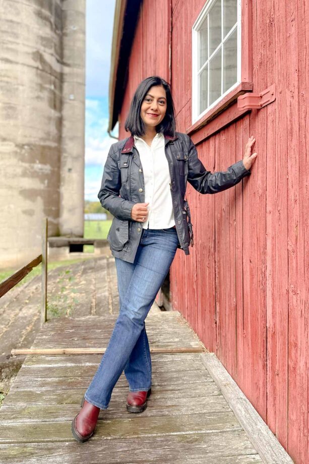 Fashionipa (Nipa) leaning against a red barn wearing a navy jacket, white shirt and blue jeans.