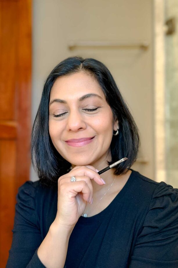 Fashionipa (Nipa) with eyes closed, holding a small angled makeup brush which she used to add brow powder to her brows.