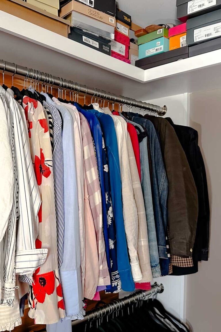 Jackets and blouses hanging in a closet. you can see a few shoe boxes on a self above.