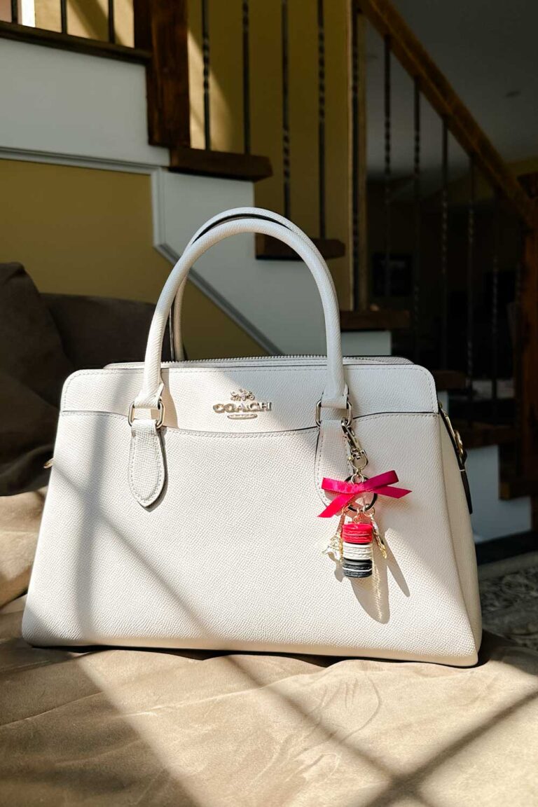 Cream Coach handbag with a charm that features stack of macarons, a pink ribbon, and a miniture Eiffel tower.