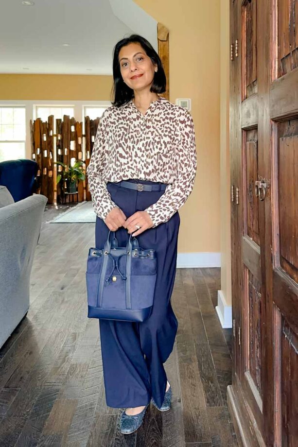 Fashionipa wearing an animal print blouse, navy pants and a navy bucket bag.