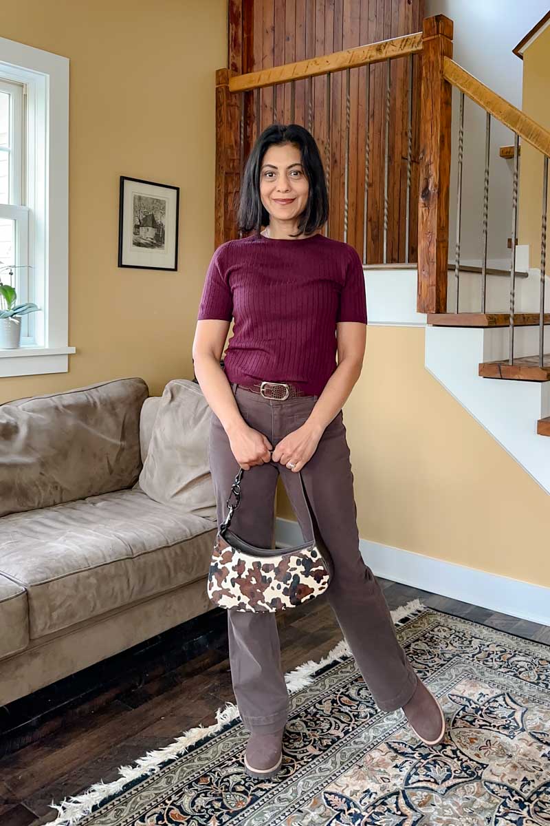 Fashionipa (NIpa) wearing a burgundy ribbed short-sleeve sweater with brown jeans, carrying a cow print handbag.