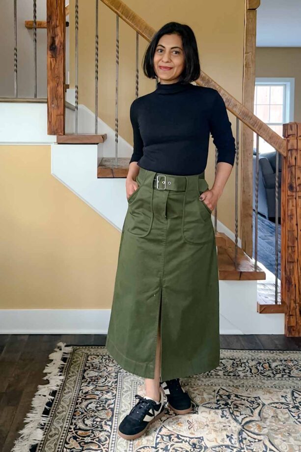 Fashionipa (Nipa) wearing a black mock-neck t-shirt with an olive a-line midi skirt and black suede sneakers.