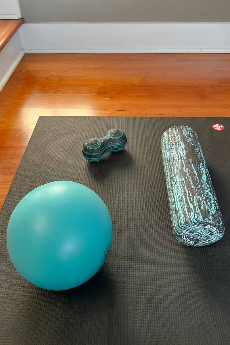 Exercise ball, foam rollers on a black yoga mat.