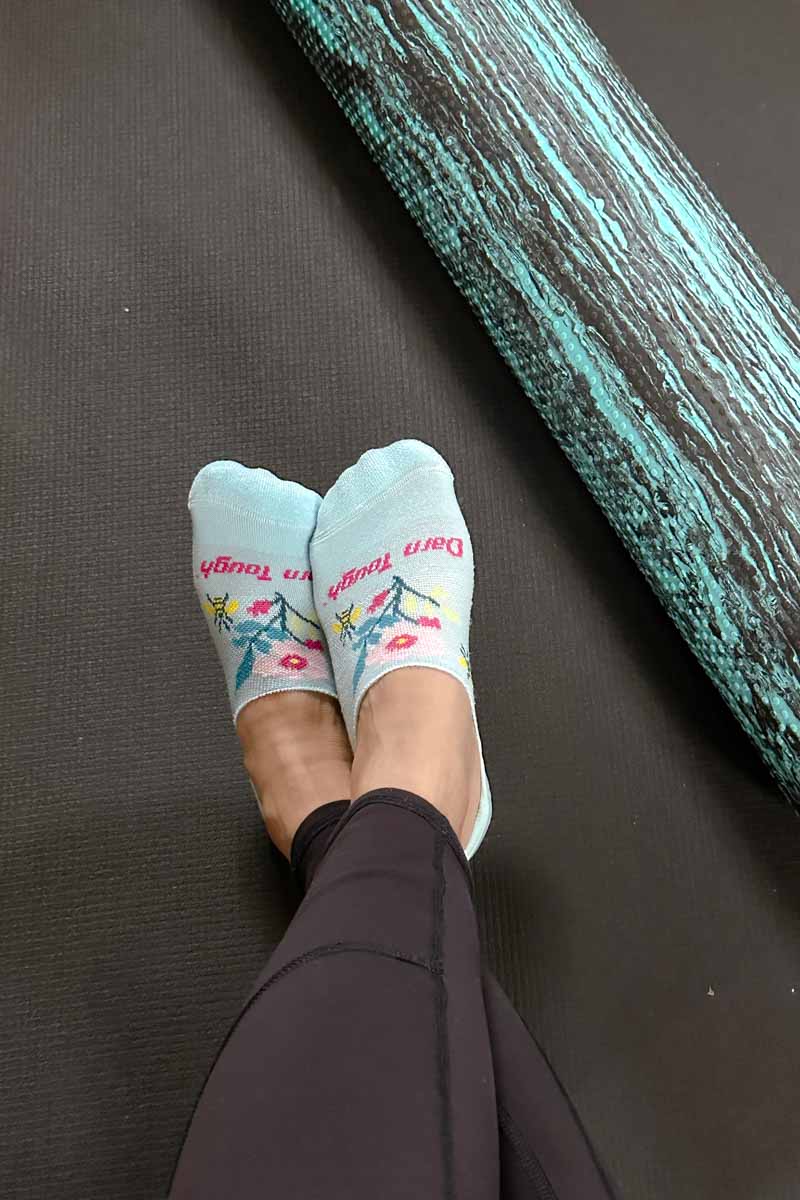 Woman's feet in Darn Tough No Show socks resting on a yoga mat next to a foam roller.