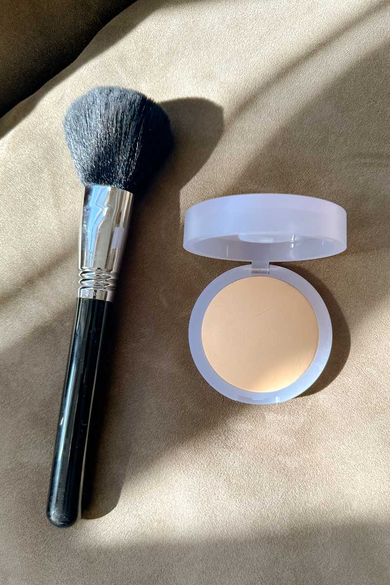 KOSAS setting powder and a large fluffy makeup brush on a tan surface.