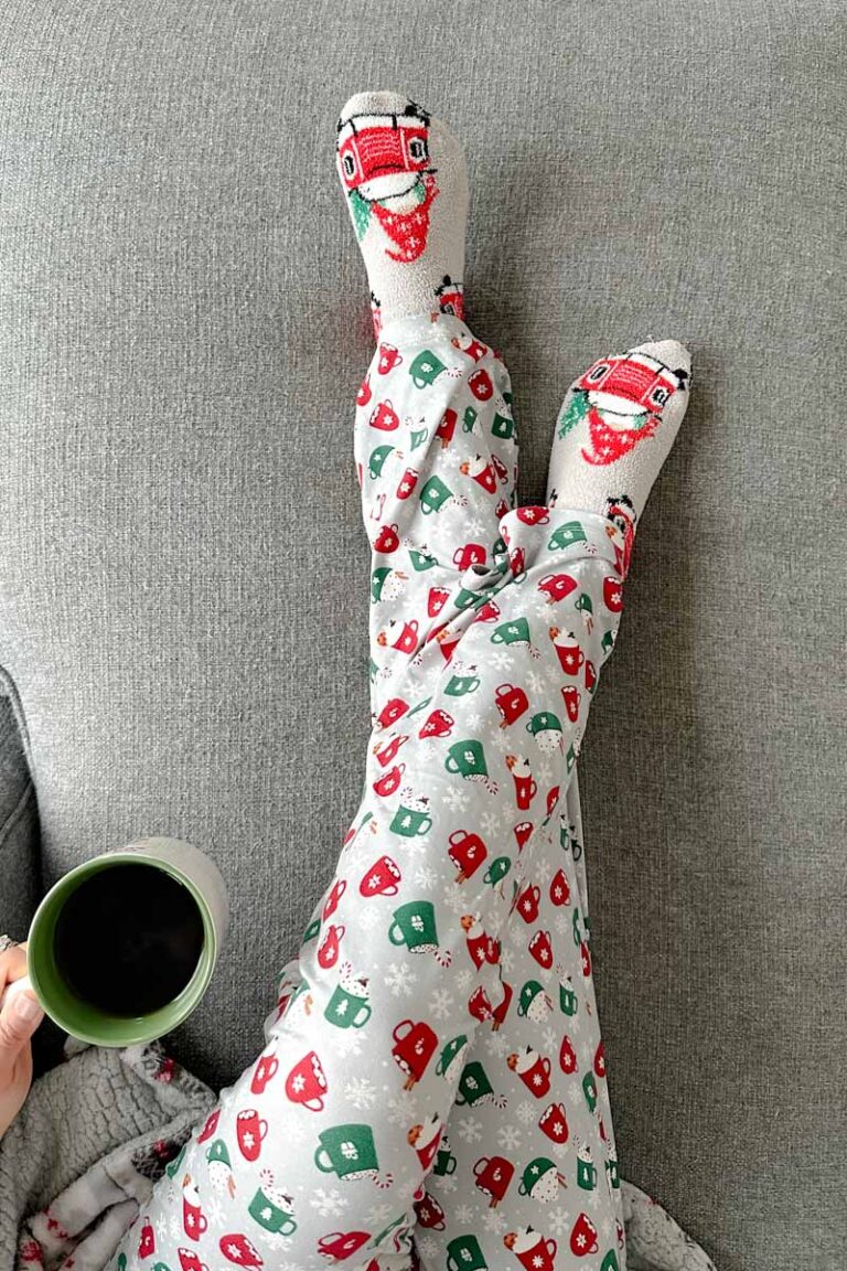 Birds eye view of a woman's legs in hot chocolate print pajamas sitting on a couch with a mug of tea.