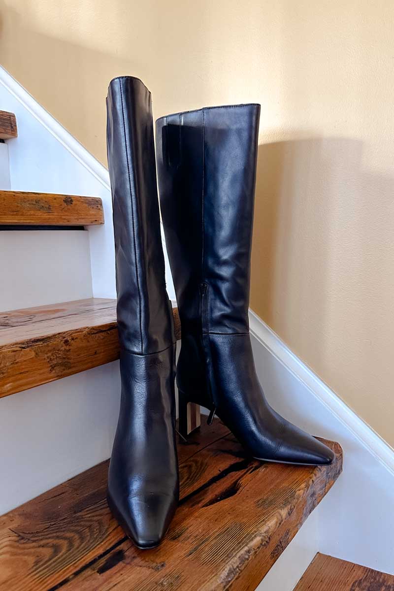 Black leather knee-high boots on wooden stairs.
