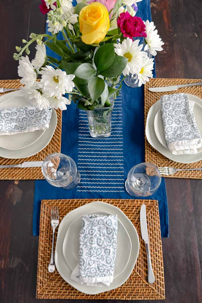 Table setting with wavy places, basketweave placemats, cotton napkins and a vase of flowers.