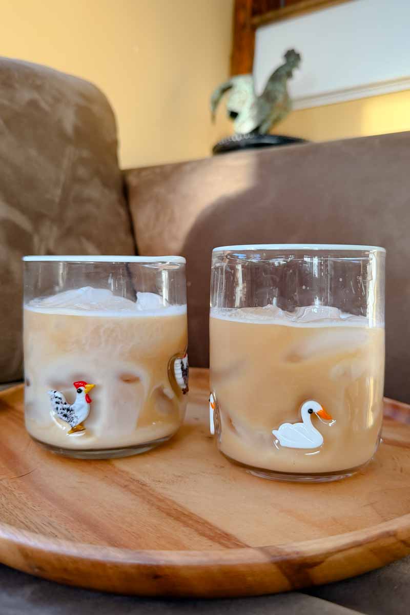 Two juice glasses with rooster and swan icons on a wooden tray.