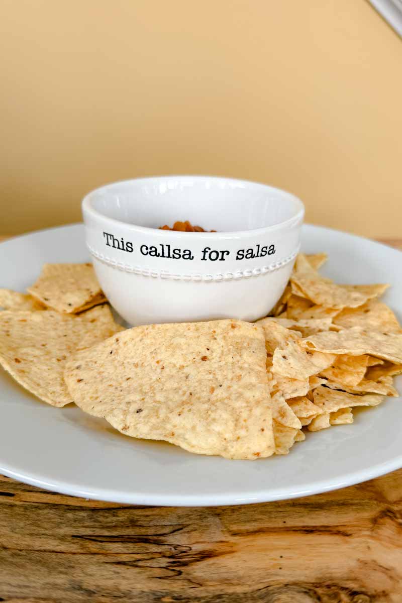 Bowl of salsa (with the words "this callsa for salsa") on a platter of tortilla chips.