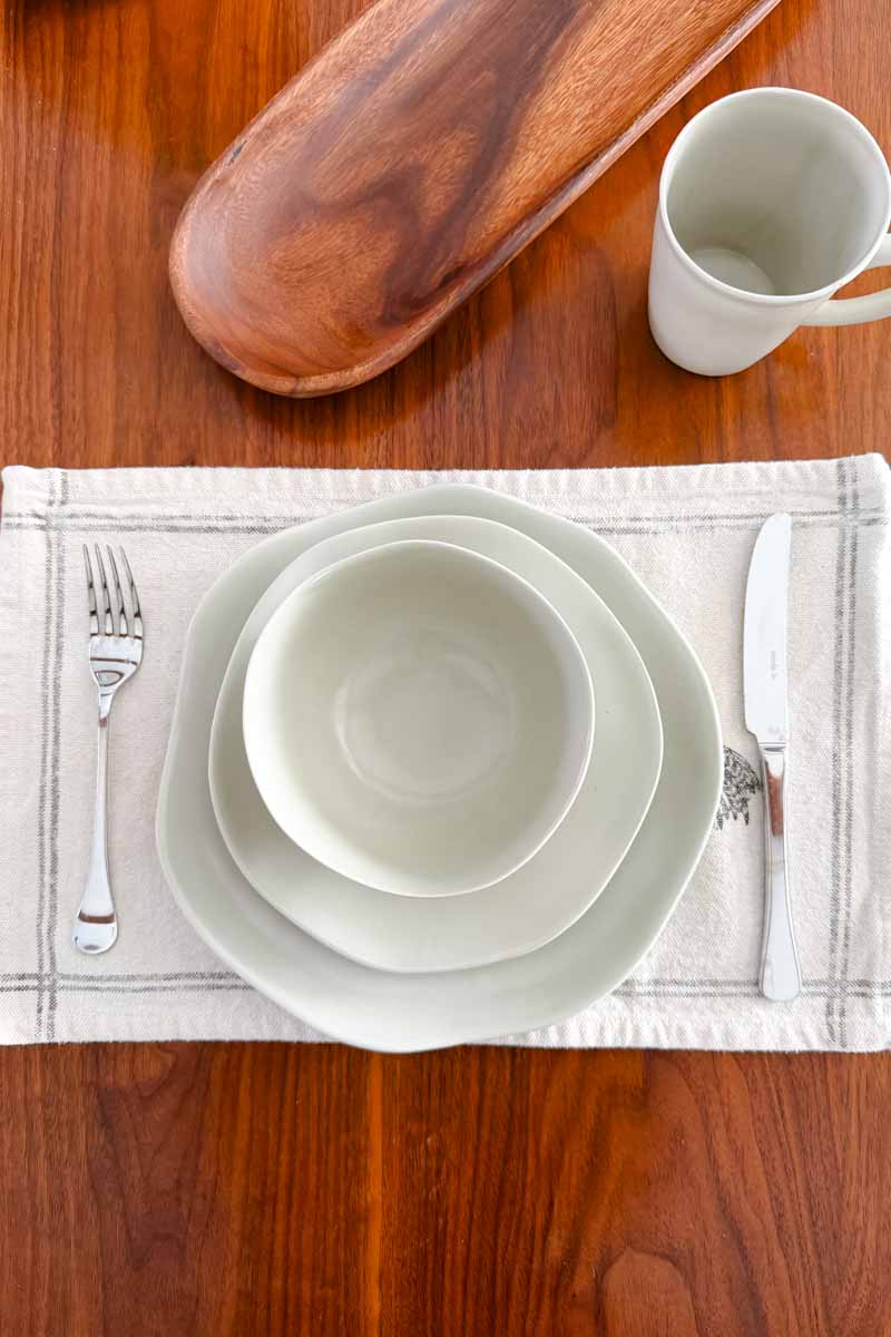 Place setting with wavy plates, silverware and a textured canvas mat.