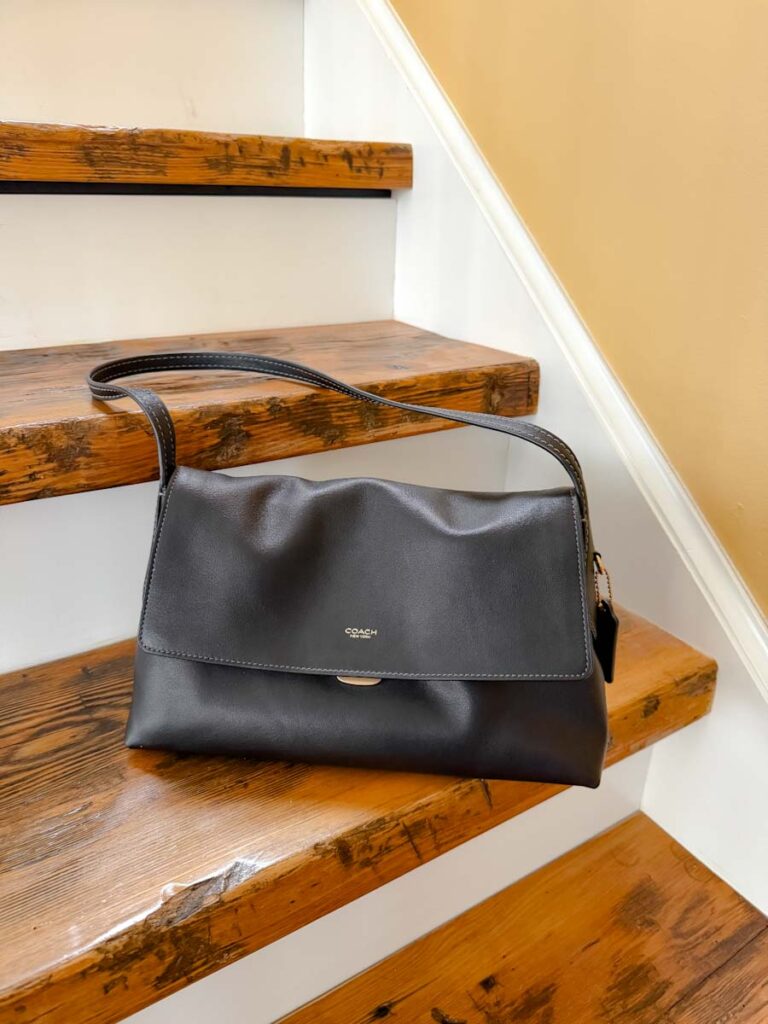 Coach Chelsea 30 in black on a wooden step.