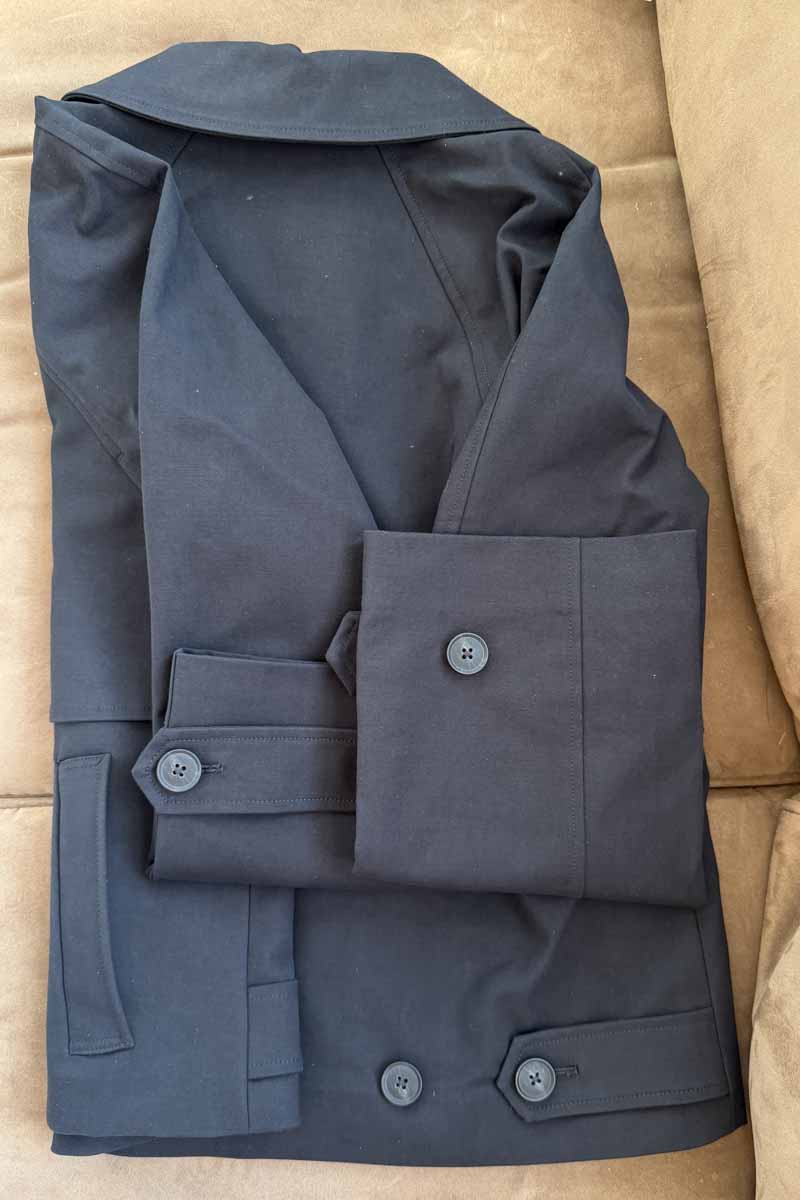 A black cropped trench coat, folded to show the adjustable buttons on the sleeve and back.