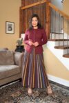 Fashionipa (Nipa) wearing a striped knit maxi dress and burgundy sweater jacket, standing next to a couch and staircase.