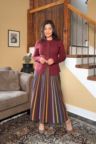 Fashionipa (Nipa) wearing a striped knit maxi dress and burgundy sweater jacket, standing next to a couch and staircase.