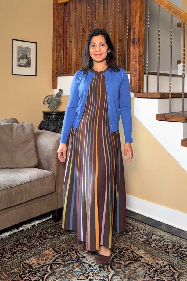 Fashionipa (Nipa) wearing a striped knit maxi dress and blue cardigan, standing next to a couch and staircase. 