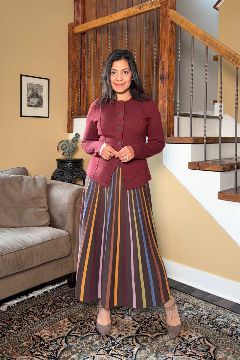 Fashionipa (Nipa) wearing a striped knit maxi dress and burgundy sweater jacket, standing next to a couch and staircase.
